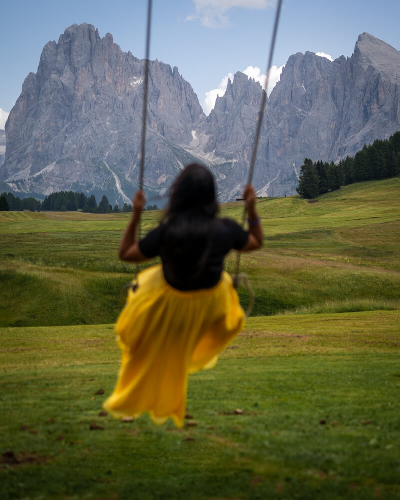 A girl in a yellow skirt on a swing at the Malga Sanon Hut in Alpe Di Siusi in the Dolomites in Italy