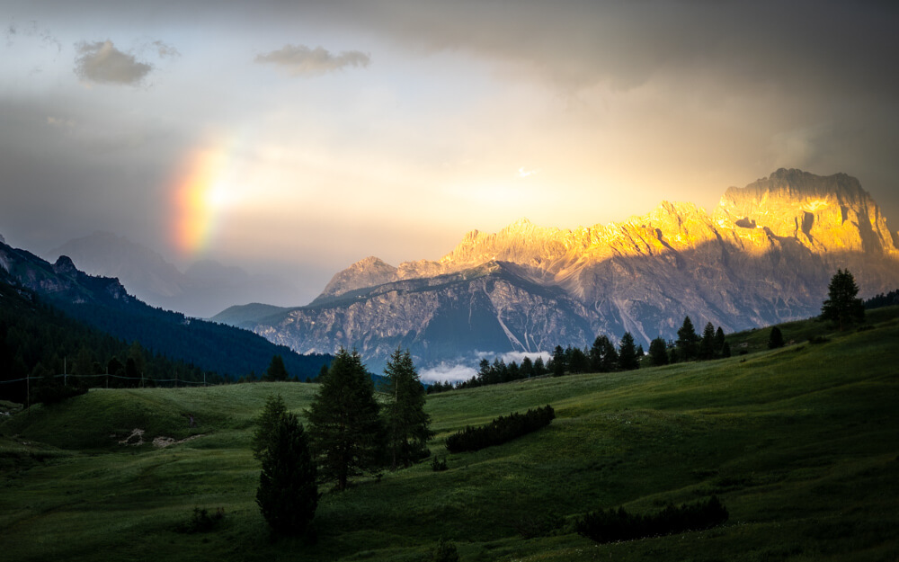 A ray of light come from a rainbow and lighting up a mountain in the Dolomite after a storm