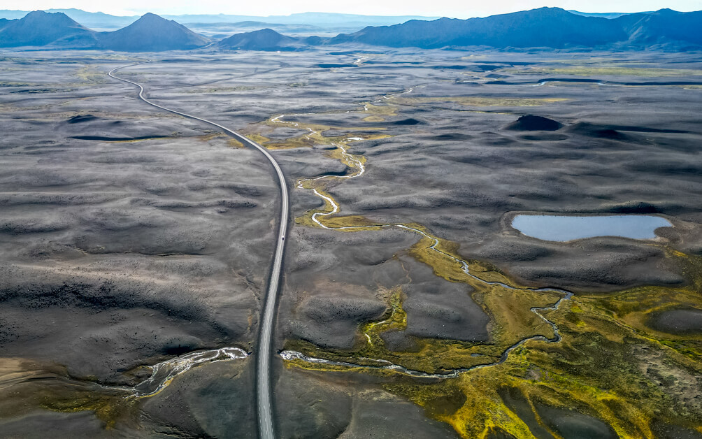 10-Day Iceland Itinerary: An Unforgettable Road Trip 50 Drone view of a roadway in iceland on our 10-day Iceland ring road trip. The road goes through black volcanic scenery with hints of green in the ground