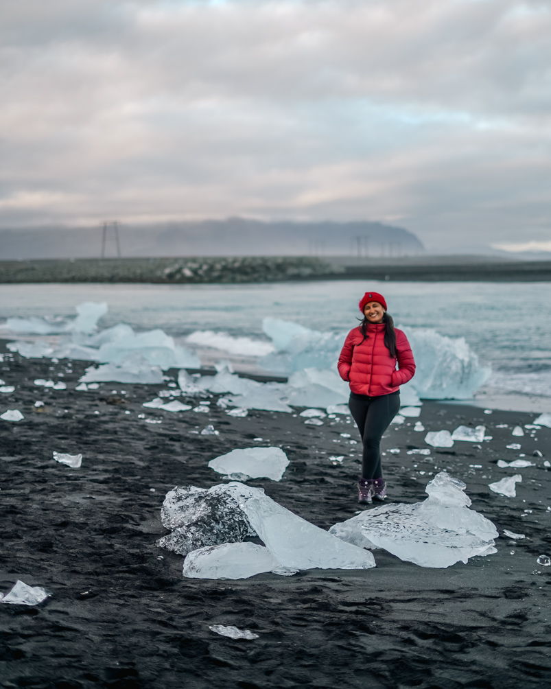 10-Day Iceland Itinerary: An Unforgettable Road Trip 38 Me posing on Iceland's Diamond Beach with several pieces of ice strewn all over