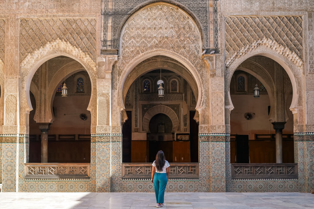 A girl stands infront of archways with traditional Moroccon architecture in a madrasa in Fes