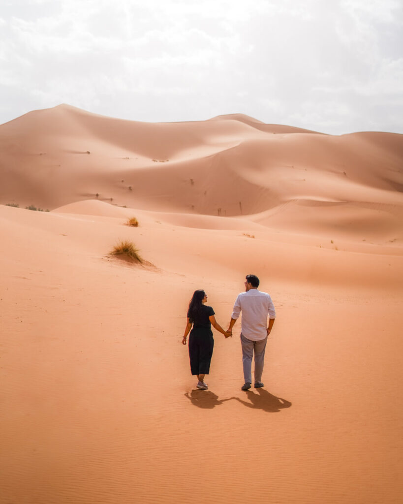 A couple walking hand in hand in the Sahara Desert in with a view of the dunes of Erg Chebbi near Merzouga in Morocco