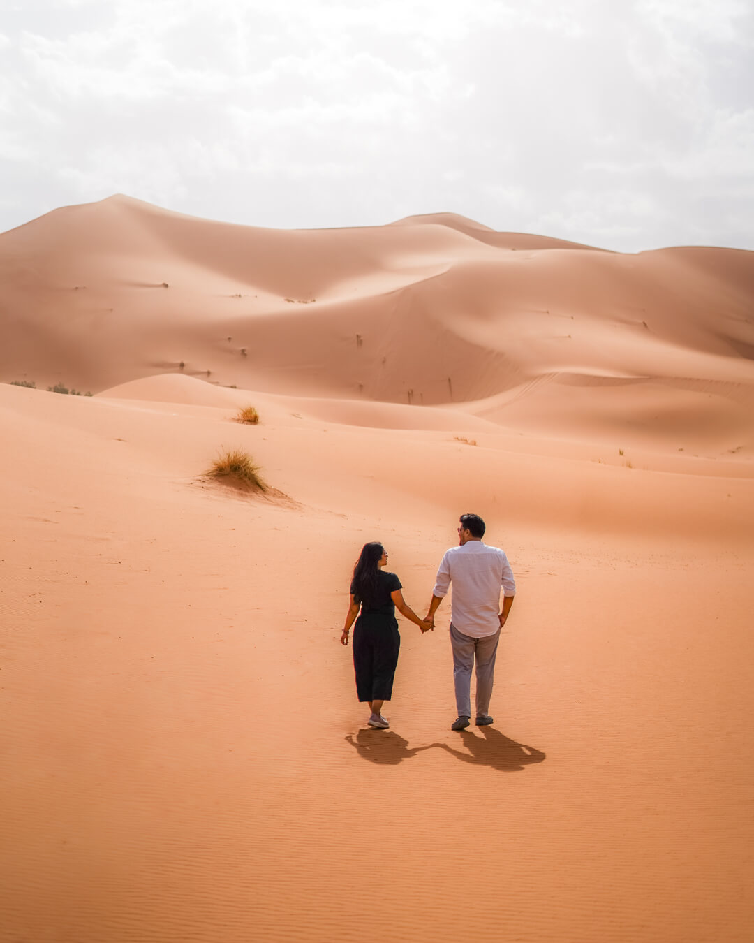 A couple walks in the desert with a background of rolling sand dunes in Merzouga 