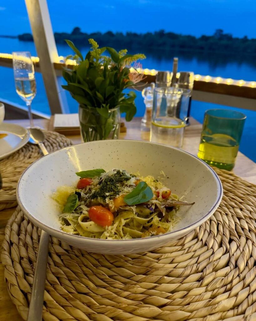 The Perfect 3 Days Victoria Falls Itinerary and Guide 13 A table with bowl of delicious pasta and a view of the river beyond
