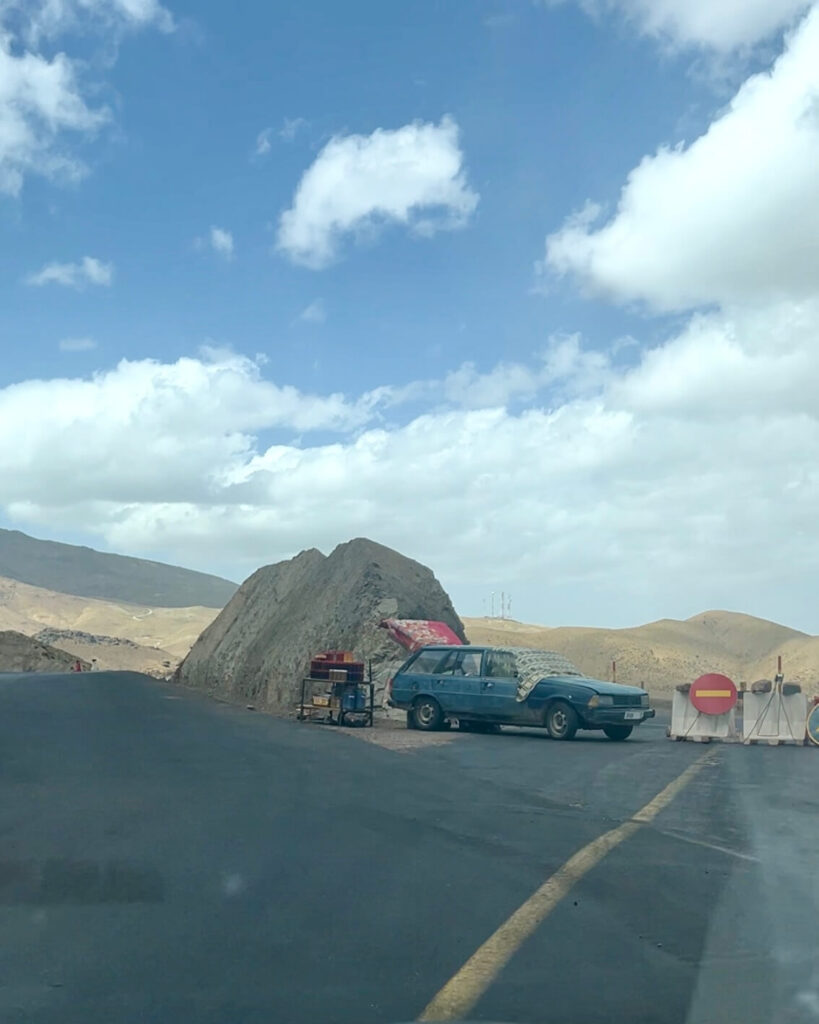 Driving in Morocco: Tips, Scams & What No One Tells You 10 A blue car selling coffee parked near a roadblock on a mountainous road in the Atlas Mountains.