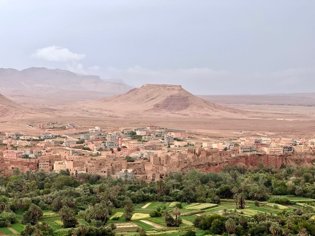Driving in Morocco: Tips, Scams & What No One Tells You 6 A Moroccan desert landscape with a flat mountain in the background and a traditional town of mud houses with greenery in the foreground.