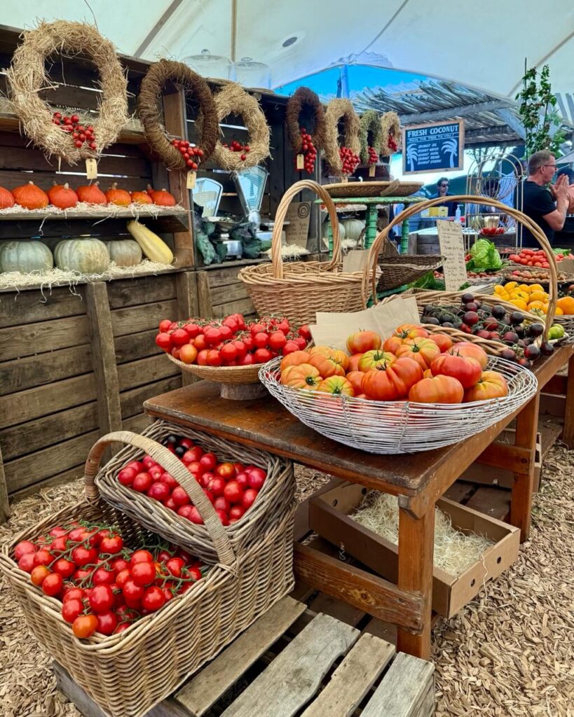 Stalls lined with vibrant produce fill a bustling outdoor Oranjezicht City Farm Market, with people browsing under the soft afternoon light—inviting and full of local charm.