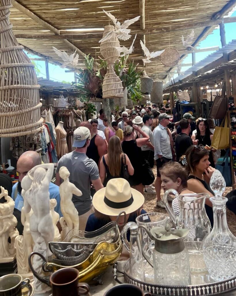 Artfully arranged stalls at the Oranjezicht City Farm Market  with colorful textiles, and local crafts sit beneath string lights, while market-goers casually stroll and shop—an inviting community vibe.
