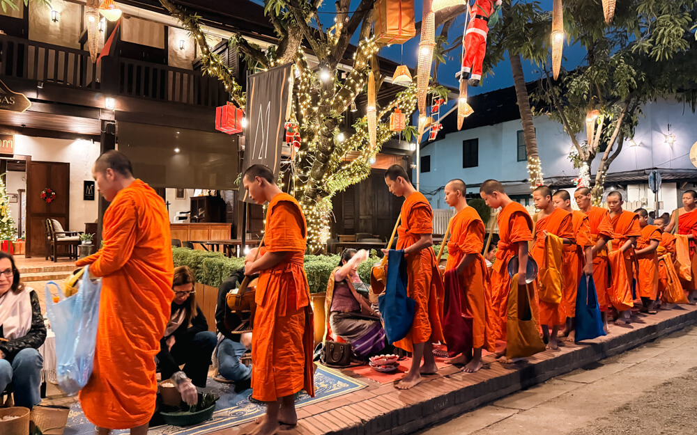 The Only Laos Itinerary You Need for 1 Week in Laos 21 Monks receiving alms at the alms giving ceremony in Luang Prabang. It's still dark (before sunrise), the street is lit up and there are people sitting on mats on the floor distributing the food.