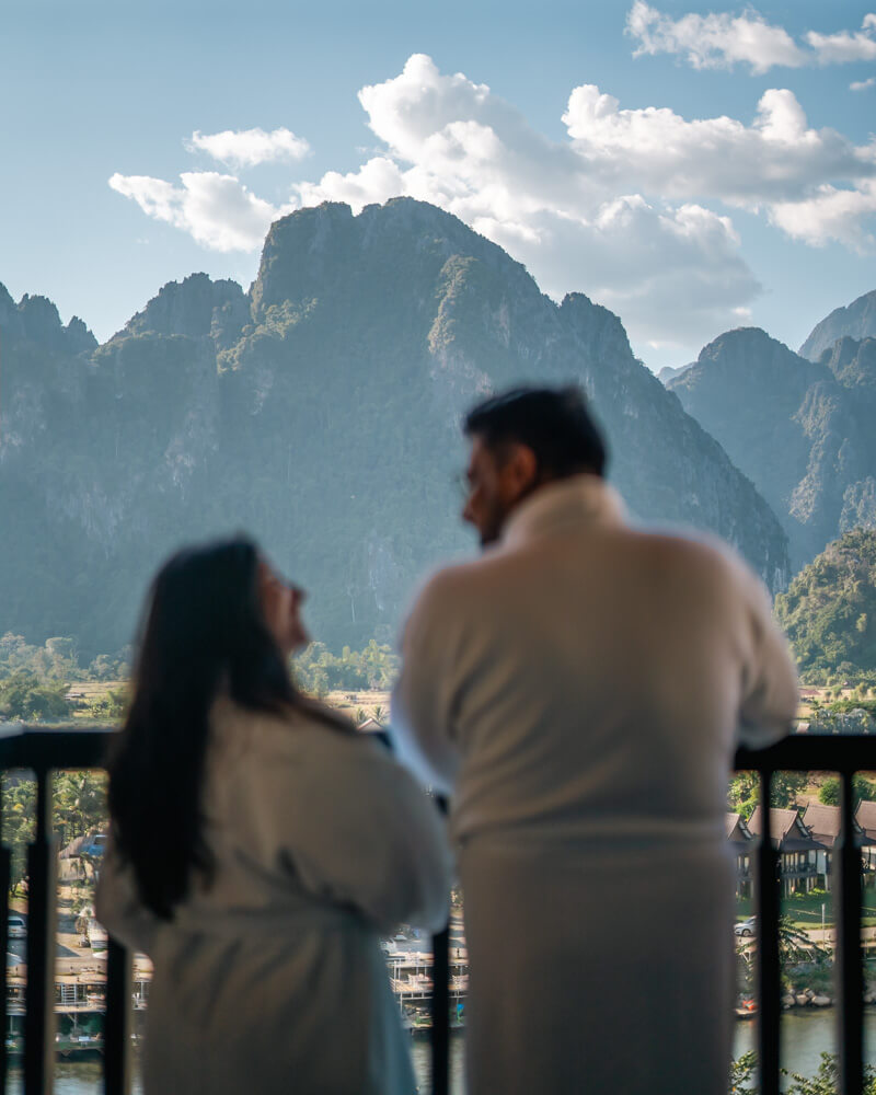The Only Laos Itinerary You Need for 1 Week in Laos 12 A couple in bath robes laughing as they enjoy the view of the mountains from their hotel balcony at Amari Vang Vieng