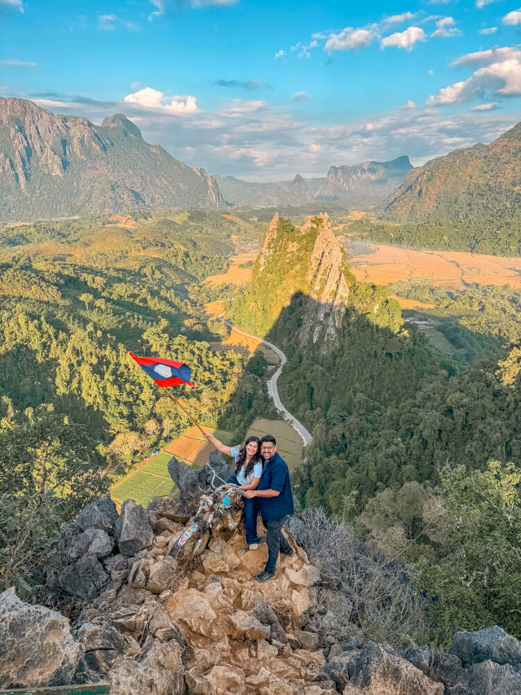 The Only Laos Itinerary You Need for 1 Week in Laos 15 A couple on a mountain top - Nam Xay Top-posing on a bike holding a flag of Laos