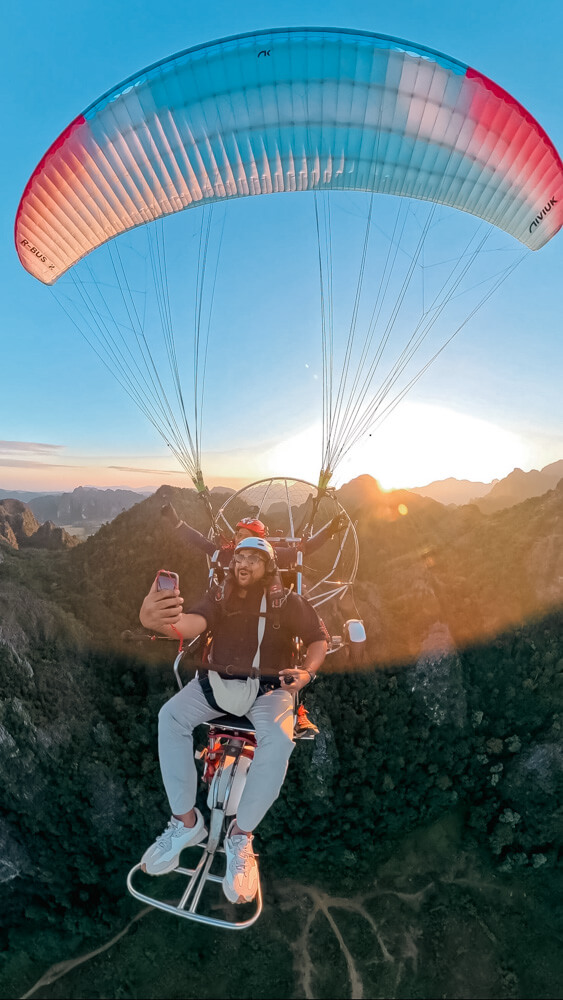The Only Laos Itinerary You Need for 1 Week in Laos 13 A man clicking a selfie of him and the pilot while paramotoring over the mountains in Vang Vieng