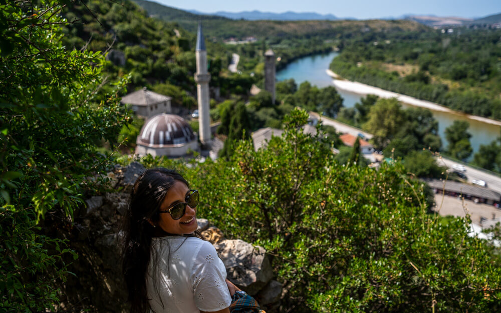 Day Trip to Mostar from Split or Dubrovnik (How to Plan It) 12 A girl looking at the camera with a view of the mosque and river in Počitelj in the background