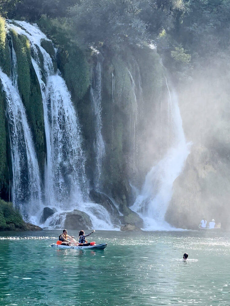 Day Trip to Mostar from Split or Dubrovnik (How to Plan It) 19 A couple kayak on emerald green waters with a view of Kravica Falls in the background