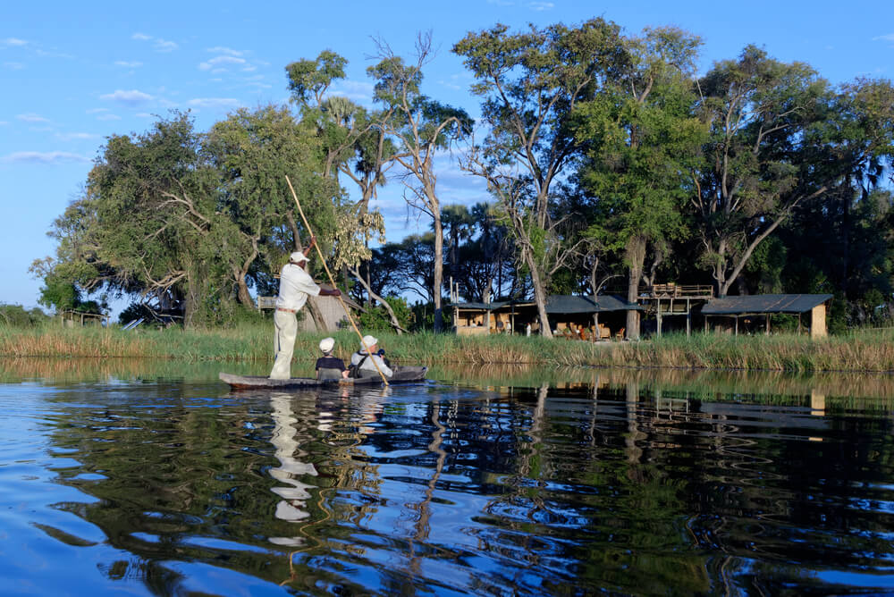 Tourists on a safari  heading to their lodge in a tradition mokoro canoe in Okavango delta in Bostwana
