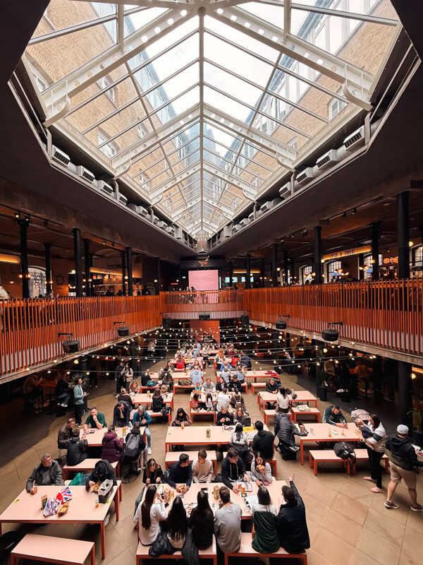 4-Day London Itinerary: Best of London + Easy Walking Routes 16 A view of the interior of Seven Dials Market with a glass skylight above, food shops on either side and people having their meal on the tables laid out below