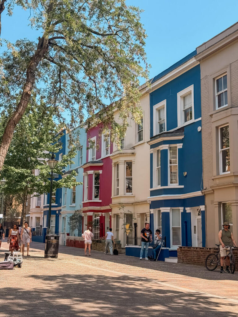 4-Day London Itinerary: Best of London + Easy Walking Routes 22 Row of colourful Notting Hill townhouses in pastel blue, red, cream, and navy, with people strolling the pavement on a sunny day.